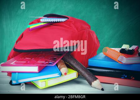 Sac rouge avec équipement scolaire sur table en bois près du tableau noir Banque D'Images