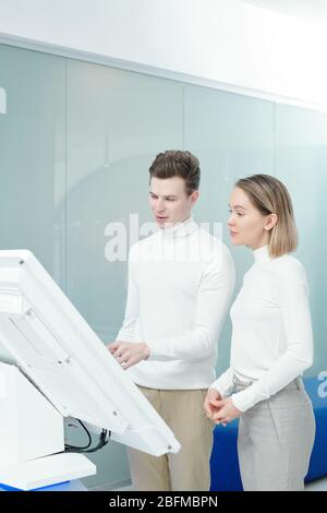 Deux jeunes développeurs futuristes de nouveaux logiciels faisant défiler des informations sur l'affichage interactif et en discutant Banque D'Images