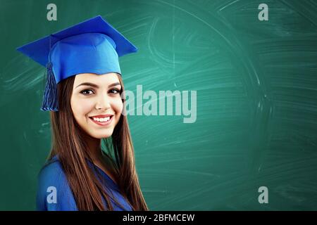 Jeune femme avec une casquette de graduation sur fond vert de tableau noir Banque D'Images