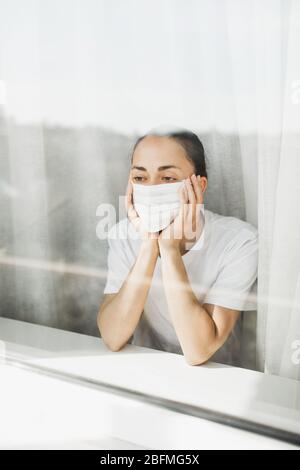 Médecin fatigué dans le masque médical regardant par la fenêtre. Travail important et auto-isolement pendant la pandémie de coronavirus. Espoir pour la médecine. Banque D'Images