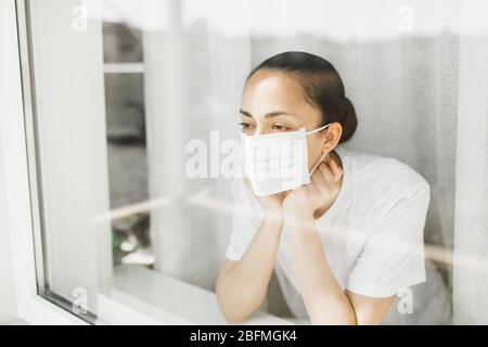 Médecin fatigué dans le masque médical regardant par la fenêtre. Travail important et auto-isolement pendant la pandémie de coronavirus. Espoir pour la médecine. Banque D'Images