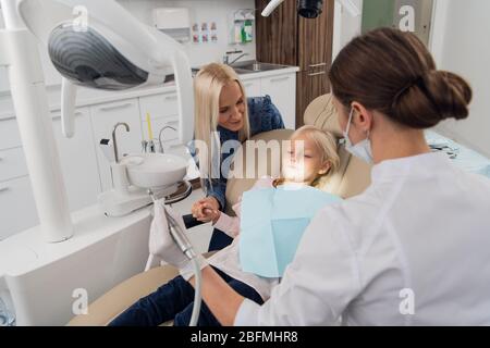 Une petite fille avec sa mère au bureau d'un dentiste. L'enfant se trouve dans la chaise, sa mère est juste à côté de sa main. Banque D'Images