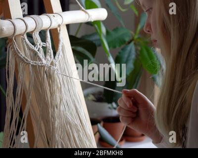 restez à la maison. travail pendant la quarantaine - une fille dans le salon tissage mural des cordes dans la technique macrame Banque D'Images