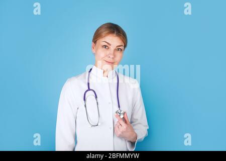 Portrait d'une jolie jeune femme médecin en blouse blanche sur fond bleu Banque D'Images