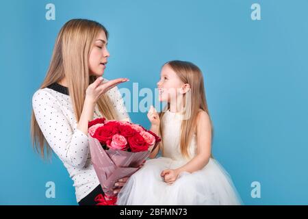 Petite fille et mère mignonne avec bouquet de fleurs sur fond bleu Banque D'Images