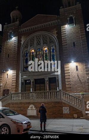 NEW YORK, NEW YORK - 18 AVRIL 2020: Le paroissiateur écoute les prières diffusées à l'extérieur d'une église orthodoxe grecque de St Demetrios fermée. Banque D'Images