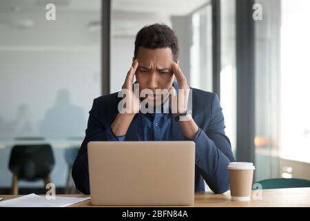 Un homme d'affaires africain assis au bureau tactile temples souffre de maux de tête Banque D'Images