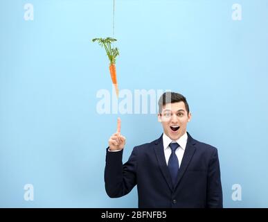 Motivation et concept d'objectif. Jeune homme pointant sur la carotte, fond bleu Banque D'Images