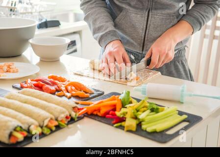 Homme caucasien préparant des petits pains à sushi faits maison. Formation de sushis. Les étapes pour créer des sushis avec du saumon. Processus de fabrication de sushis en suivant la cuisson Banque D'Images