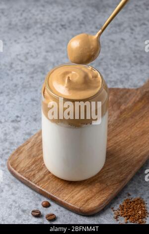 Café Dalgona en verre avec cuillère sur gris. Espresso à latte à boire coréen avec mousse de café instantané. Prise de vue verticale. Banque D'Images