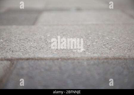 Vue étroite d'un carrelage en béton sur le trottoir flou. Bloc de ciment sur un passage pour piétons. Fond abstrait texturé bokeh. Banque D'Images