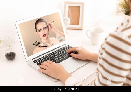 Femme regardant la formation en ligne pour l'artiste professionnel de maquillage sur ordinateur portable à la table Banque D'Images