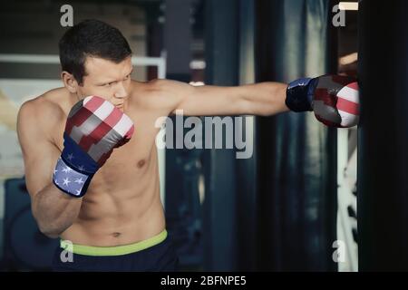 Homme avec gants de boxe de couleur aux Etats-Unis drapeau sac de poinçonnement dans la salle de gym. Concept de puissance et de force nationales Banque D'Images
