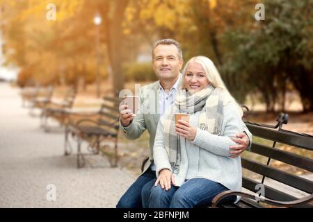 Portrait du couple d'âge mûr avec café assis sur un banc dans le parc d'automne Banque D'Images