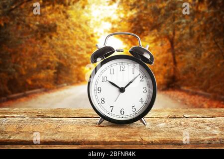 Alarm clock on wooden table against landscape background. Time change concept Banque D'Images