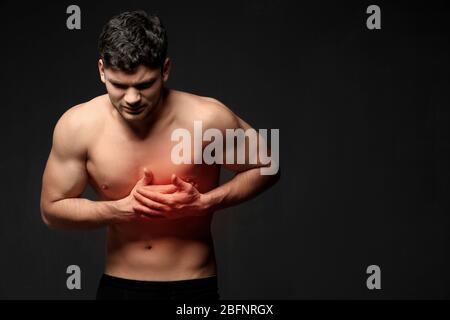 Jeune homme souffrant de douleur thoracique sur fond noir. Concept de soins de santé Banque D'Images