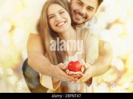 Jeune couple avec coeur dans les mains se posant sur fond flou Banque D'Images