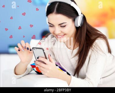 Bonne jeune femme avec casque à l'écoute de la musique sur un canapé Banque D'Images