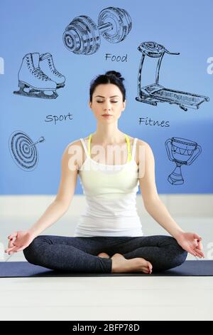 Belle jeune femme assise dans lotus pose sur tapis à la maison. Concept de style de vie sportif. Diversité des icônes sportives sur fond. Banque D'Images