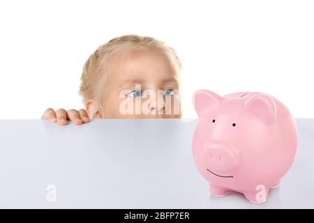 Drôle petite fille se cachant derrière la table blanche et regardant la banque de piggie de céramique rose Banque D'Images