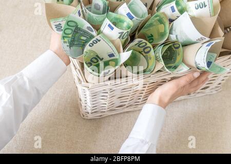 Beaucoup de factures cent euros dans le panier de Wisker blanc comme cadeau sur le fond blanc. La main contient un emballage avec de l'argent. Banque D'Images