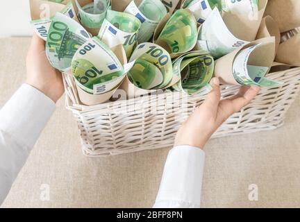 Beaucoup de factures cent euros dans le panier de Wisker blanc comme cadeau sur le fond blanc. La main contient un emballage avec de l'argent. Banque D'Images