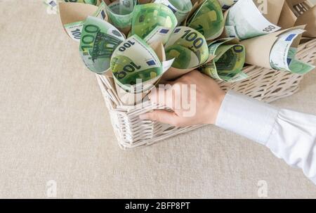 Beaucoup de factures cent euros dans le panier de Wisker blanc comme cadeau sur le fond blanc. La main contient un emballage avec de l'argent. Banque D'Images