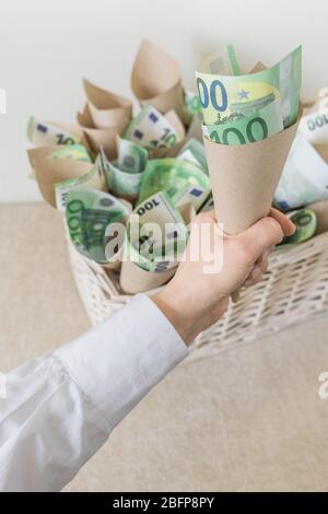 Beaucoup de factures cent euros dans le panier de Wisker blanc comme cadeau sur le fond blanc. La main contient un emballage avec de l'argent. Banque D'Images