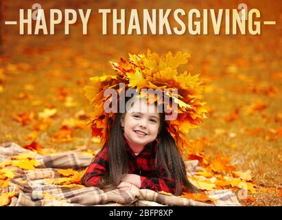 Bonne journée de Thanksgiving. Une jeune fille heureuse en couronne jaune d'automne posée sur le plaid dans le parc Banque D'Images