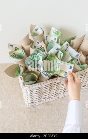 Beaucoup de factures cent euros dans le panier de Wisker blanc comme cadeau sur le fond blanc. La main contient un emballage avec de l'argent. Banque D'Images