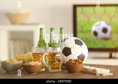 Des en-cas savoureux, de la bière et la balle sur une table de cuisine à l'arrière-plan flou Banque D'Images
