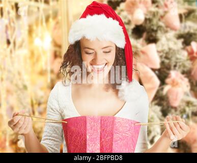 Belle femme heureuse à Santa Hat avec sac de shopping sur fond de sapin flou décoré. Concept de shopping de Noël. Banque D'Images