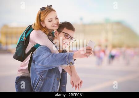 Jeune couple heureux prenant selfie sur fond flou de la place de la ville. Banque D'Images
