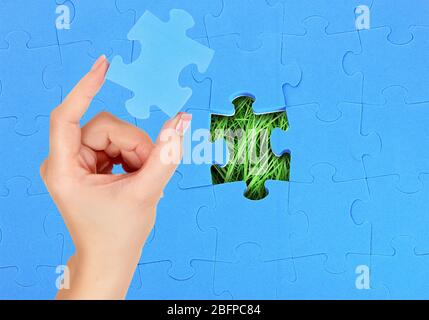 Main féminine avec pièce de puzzle manquante. Le museau bleu sur l'arrière-plan de l'herbe verte. Banque D'Images