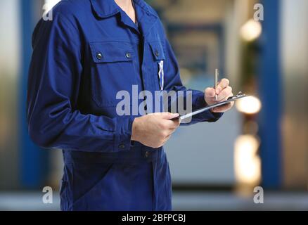 Mécanicien en uniforme avec presse-papiers et stylo sur station-service fond flou Banque D'Images