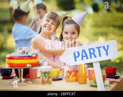 Mignons petites filles à la fête d'anniversaire. Fête de mot sur panneau en bois contre fond de fête flou Banque D'Images