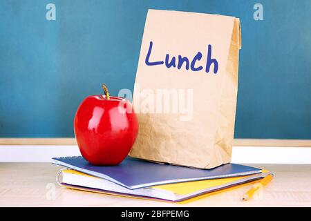 Concept de déjeuner scolaire. Sac en papier, pomme et papeterie sur table en bois Banque D'Images