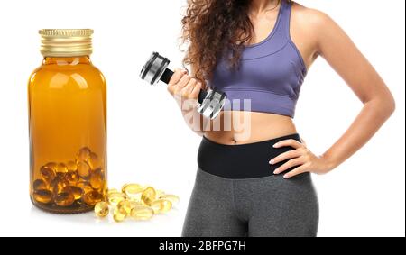 Concept d'huile de poisson pour perte de poids. Jeune femme sportive avec haltère et capsules sur fond blanc Banque D'Images