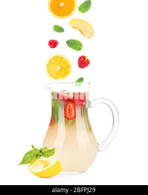 Chute de tranches de fruits et de baies dans une verseuse en verre avec limonade sur fond blanc. Recette pour une boisson d'été Banque D'Images