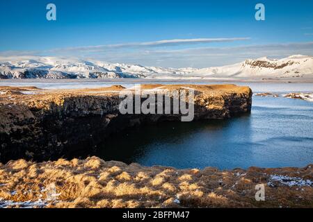Falaises et mer avec des montagnes enneigées derrière à Dyrhólaey dans le sud de l'Islande Banque D'Images