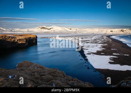 Falaises et plage de sable noir avec des montagnes enneigées derrière à Dyrhólaey dans le sud de l'Islande Banque D'Images