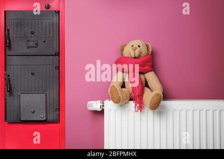 Concept d'économies d'énergie. Chaudière à combustible solide et radiateur avec ours en peluche sur fond de couleur Banque D'Images