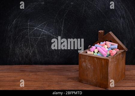 Boîte en bois de craie colorée sur table contre le tableau noir de l'école Banque D'Images