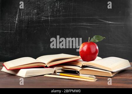 Livres et pomme sur table en bois contre le tableau noir de l'école Banque D'Images
