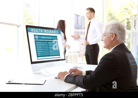 Homme senior travaillant avec un ordinateur au bureau. Concept d'assurance maladie Banque D'Images