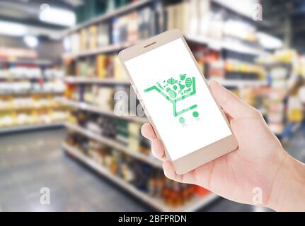 Femme tenant son smartphone et ses étagères floues avec différents produits en arrière-plan. Concept de shopping sur Internet Banque D'Images