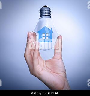 Femme tenant une ampoule avec modèle de maison à l'intérieur sur fond couleur. Concept de consommation d'énergie Banque D'Images