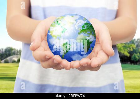 Petit enfant tenant le globe dans les mains et paysage sur fond. Concept d'aide Banque D'Images