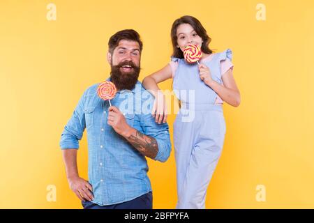 Temps doux. Fond jaune de famille de dents douces. Un père heureux et une fille tiennent des bonbons. Homme barbu et petit enfant. Friandises. Boutique de bonbons. Confiseries à base de sucre. Les meilleures choses dans la vie sont douces. Banque D'Images