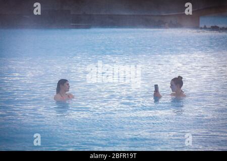 Deux femmes bavarder dans la piscine thermale de Blue Lagoon près de Reykjavik en Islande avec de la vapeur qui s'en est découpée par une journée froide en hiver Banque D'Images